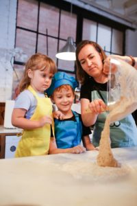 mother pouring dough out of a bowl, enjoying cooking together with her two young children