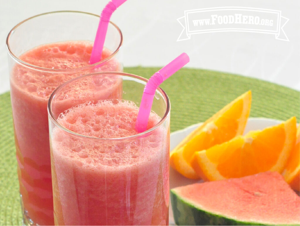 2 glasses of watermelon cooler with straws next to plate of fresh orange and watermelon slices